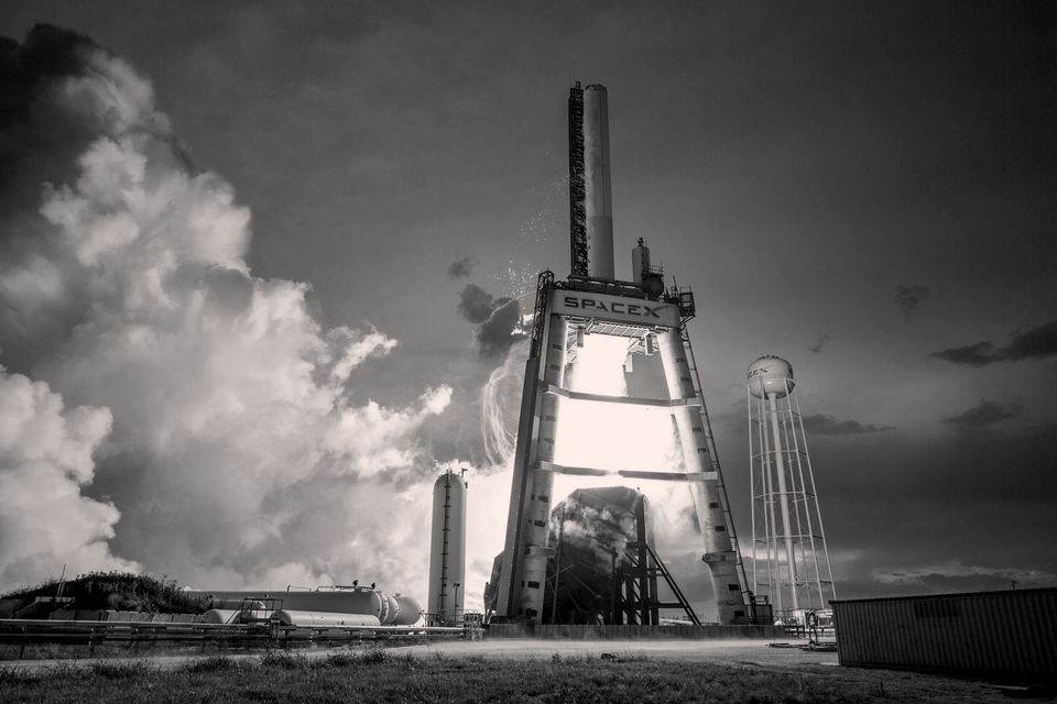 An aerospace launch structure under a dramatic sky, in black and white